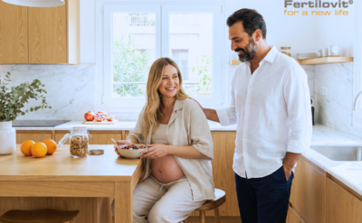 Ένα χαμογελαστό ζευγάρι σε μια ηλιόλουστη κουζίνα με τη μέλλουσα μητέρα να απολαμβάνει ένα υγιεινό γεύμα, συμβολίζοντας τη σημασία της χολίνης και της ευφυΐας του μωρού μέσω της σωστής διατροφής και του Fertilovit For2 Plus DHA.